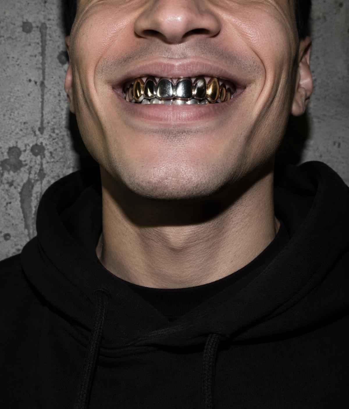 Smile wearing mixed silver and yellow gold grillz against a raw concrete wall